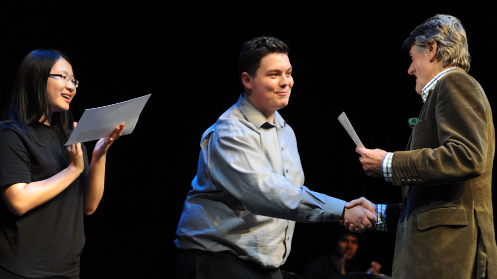 Scott Griffin, créateur des Voix de la poésie, présente son certificat de participation et son chèque de $5000 à Jonathan Welstead, champion de l’édition 2011 du concours, sous les applaudissements d’Anna Jiang.